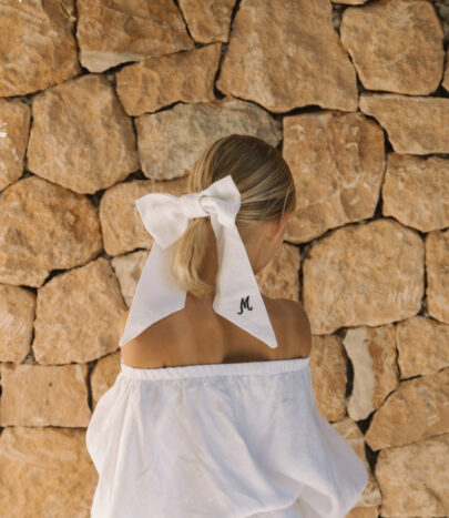 A girl aged around 10 years old with a white linen hair bow with long tails and her initial embroidered on it in black.